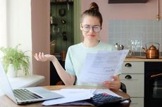 A woman looks at a piece of paper while frowning. 