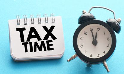 TAX TIME words in a notebook next to an alarm clock on a blue background.