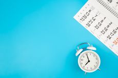 small alarm clock with corner of a calendar and bright teal backdrop