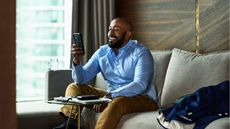 A man sitting on his sofa smiles as he looks at his smartphone.