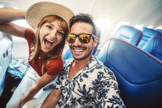 A happy couple takes a selfy on an airplane, headed to a beach vacation.