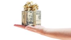 A gift box wrapped in a fifty-dollar bill with a bow sits on a woman's palm.