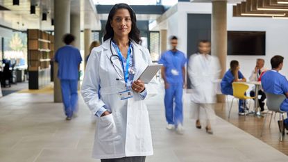 A doctor looks steady with a clipboard in a busy hospital hallway.