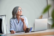 A woman sitting at a desk with a laptop wearing glasses and looking off in the distance.