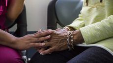 A young nurse holds hands with an older adult, only their hands showing.