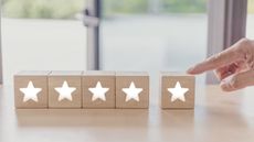 Five wooden blocks with white stars on them are lined up while a woman points at the last one, only her hand showing.