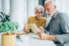 Shot of cheerful mature couple sitting on the table at home and using digital table