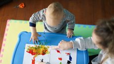 An overhead view of a nanny showing a toddler how to paint.